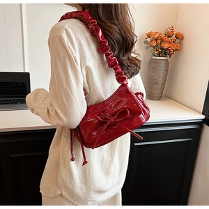 Dettaglio borsa baguette in vernice rossa con fiocco e tracolla cloud plissettata