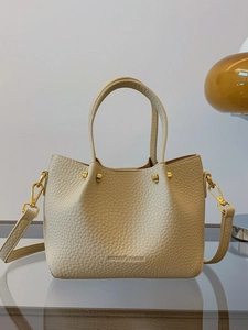 Minimalist beige pebble leather bucket bag with top handles and a gold-tone hardware finish