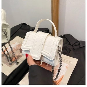 Close-up of a white mini handbag featuring crocodile pattern and metallic chain strap
