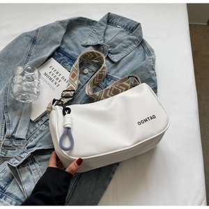 White shoulder bag detail featuring ethnic style woven strap and blue knot pendant accessory