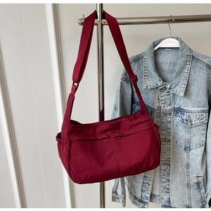 Detail of dark red nylon crossbody bag with adjustable wide strap and drawstring side pocket