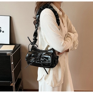 Detail of black glossy PU underarm bag featuring ribbon bow and pleated shoulder strap