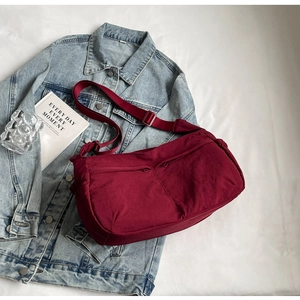 Detail view of burgundy nylon crossbody bag with dual zipper pockets on denim background