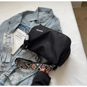 Detail of black crossbody bag with geometric woven strap on casual denim jacket