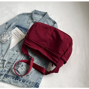 Detail view of burgundy nylon crossbody bag on denim jacket with lifestyle props