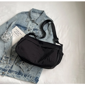 Detail view of black nylon crescent crossbody bag on blue denim jacket background