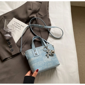 Close-up of light blue textured tweed handbag with cute silver balloon dog charm detail