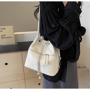 Detail of cream white patent leather bucket bag with ribbon buckle and pearl drawstring
