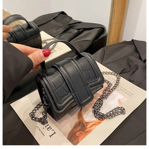 Close-up of black crocodile pattern mini bag with gun-metal chain on mirror surface