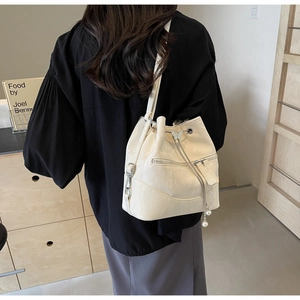Detail of cream bucket bag showing drawstring closure, pearl charm, and butterfly buckle