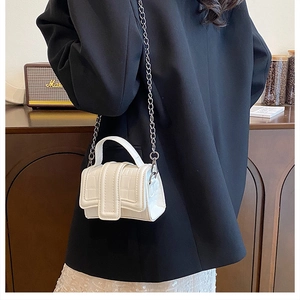 Detail view of mini white crossbody bag with crocodile texture and silver chain