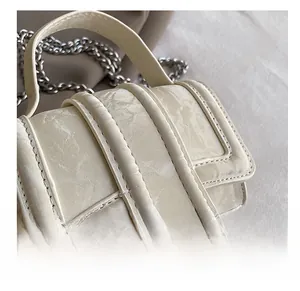 Macro detail of cream mini bag showing cracked marble texture and silver chain strap