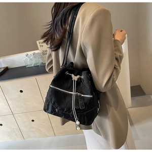 Detail of black drawstring bucket bag featuring butterfly metal buckle and pearl tassels