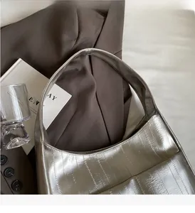 Détail du cabas argenté métallisé avec texture gaufrée verticale sur fond de blazer
