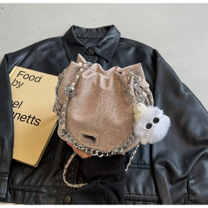 Detail of beige drawstring bucket bag with silver chain and white plush charm on leather