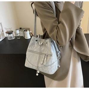 Detail of light gray drawstring bucket bag with silver butterfly and pearl accents