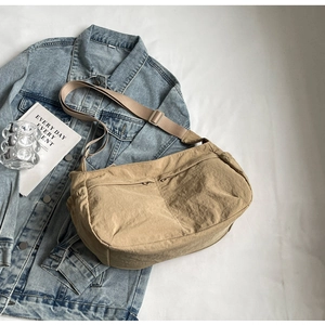 Flat lay of khaki nylon crossbody bag with dual zip pockets on white backdrop with props