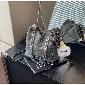 Detail of grey washed denim bucket bag with silver chain and white plush monster charm