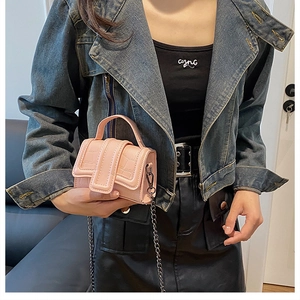 Detail view of pink crocodile-embossed mini square bag with silver chain strap on model