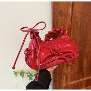 Dettaglio borsa in pelle verniciata rossa con fiocco decorativo e tracolla a pieghe