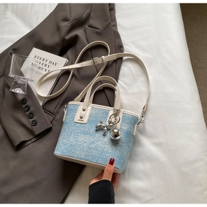 Detail of light blue denim tote bag with white trim, silver rivets and balloon dog charm