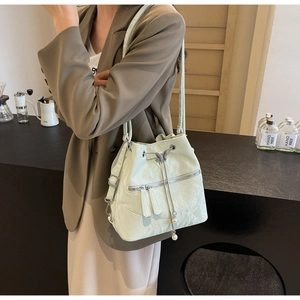 Detail view of mint green bucket bag featuring metal butterfly charms and pearl drawstring