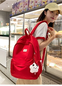 Side view of large red backpack featuring bear embroidery and star panda plush charm