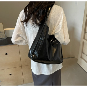 Vue arrière d'un mannequin portant un grand sac à bandoulière noir en cuir verni brillant