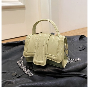 Detail view of mini green square bag with silver chain strap and top handle on leather jacket