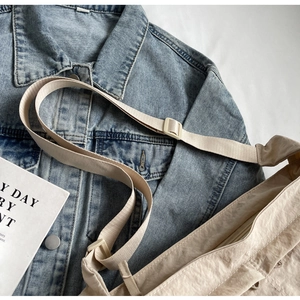 Close-up of beige nylon crossbody bag with adjustable strap on denim jacket background