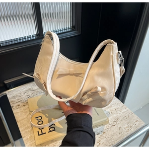 Close-up of off-white hobo bag with bow details held in a modern lifestyle setting