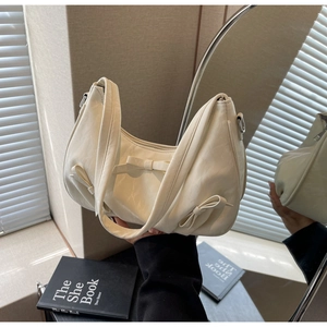 Close-up of cream textured leather handbag featuring decorative bows and metal zippers