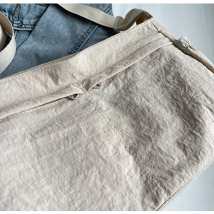 Detailed close-up of beige waterproof nylon crossbody bag with exterior zipper pocket