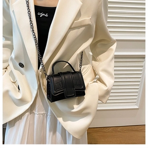 Close-up of black crocodile pattern mini bag with chain strap on white outfit