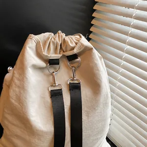 Detalle de anillas en D plateadas y correas de nailon negro en bolso de tela color beige
