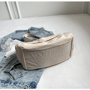 Minimalist beige dumpling tote bag with soft pleated nylon texture shown on white sheets