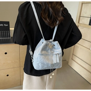 Detail of light blue bucket backpack with drawstring, butterfly buckle, and pearl tassels