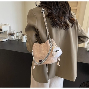 Detail of minimalist bucket bag with chain strap and plush pendant on model