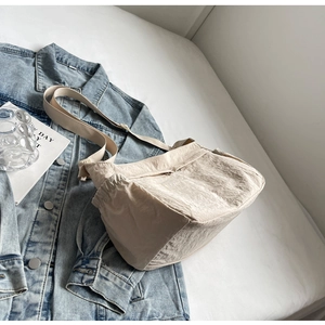 Detail of beige nylon crossbody bag with drawstring on denim jacket background
