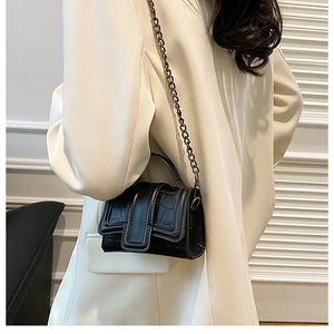 Close-up of black crocodile pattern mini square bag with metal chain on a white blazer