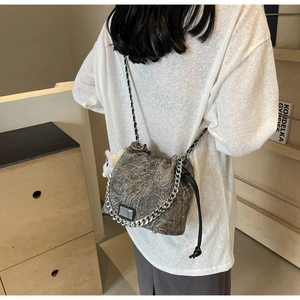 Detail of grey bucket bag with silver chains and plush pendant on model in home setting