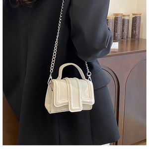 Close-up of cream mini square bag with metal chain strap on a black blazer