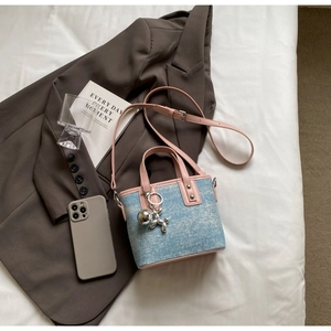 Detail of pink leather handles and blue denim texture on a bucket bag with dog charm