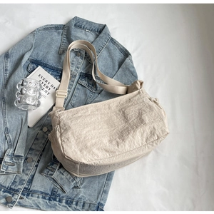 Flat lay view of a cream dumpling bag with pleated nylon fabric and adjustable strap