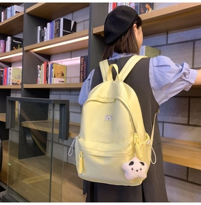 Close-up of a light yellow nylon school backpack with bear print and star plush pendant