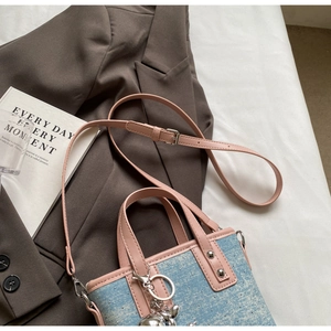 Detailed close-up of blue polka dot denim bucket bag with pink leather trim and bear charm