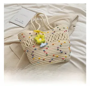 Détail du cabas en paille tissée avec pompons colorés et pendentif fleur jaune déco