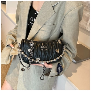 Detail of black pleated leather crossbody bag featuring silver chain and metal skull charms