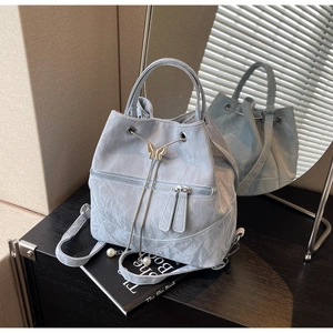 Detail of light blue bucket backpack featuring butterfly metal buckle and pearl charms
