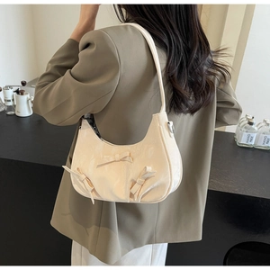 Detailed view of beige crescent bag with decorative bows on a model's shoulder